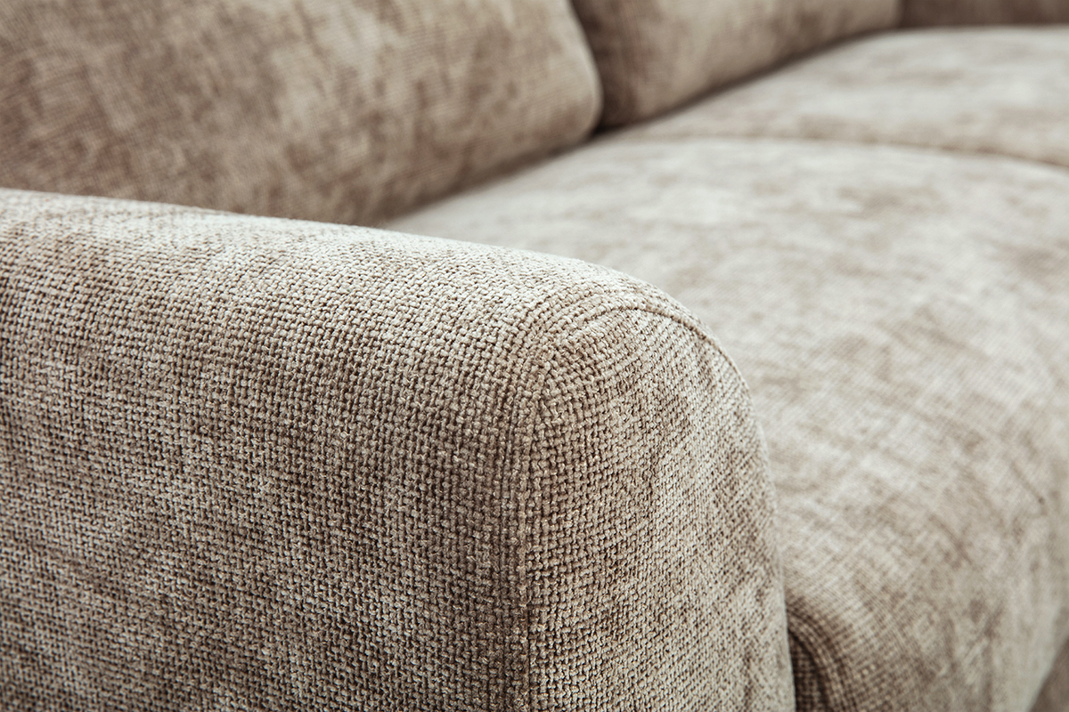 Gros plan sur l'accoudoir d'un canap� 3 places en tissu effet velours textur� taupe.