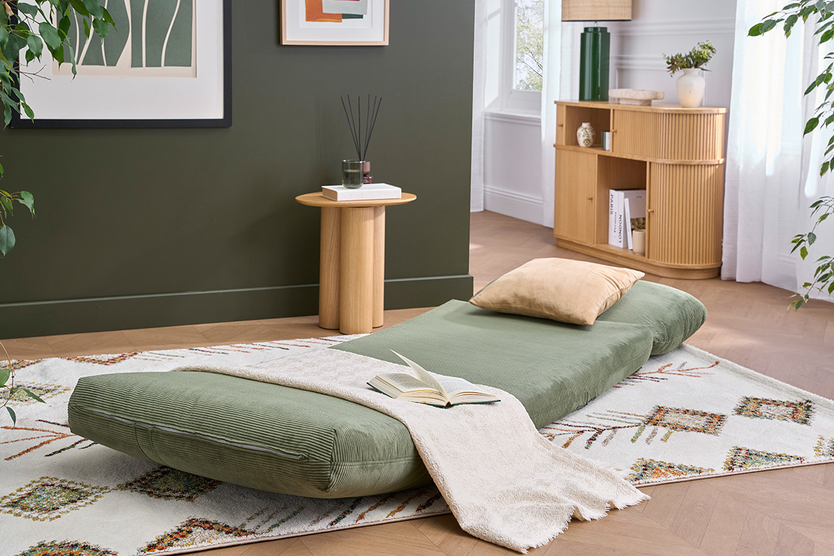 Chauffeuse SPENCER en velours c�tel� vert kaki d�pli�e en lit, sur un tapis, avec coussin beige.