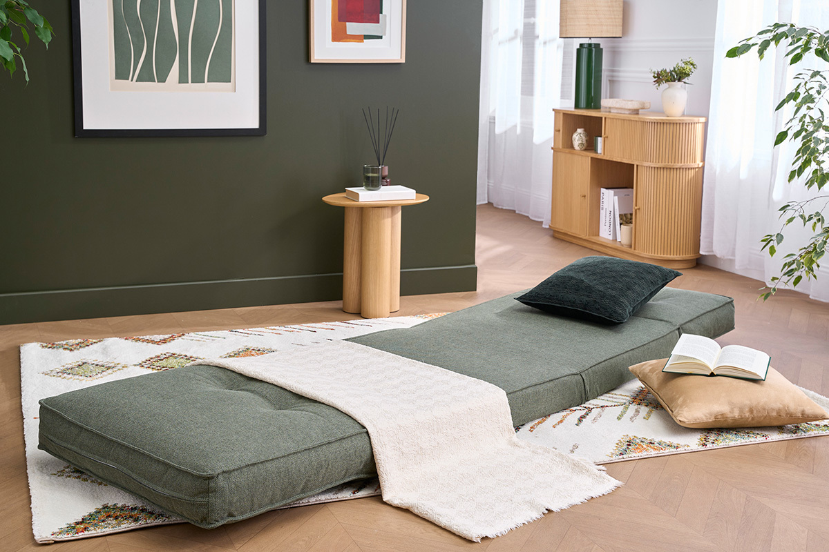 Chauffeuse SALLY convertible en tissu vert kaki, d�pli�e, avec coussins et plaid sur tapis.