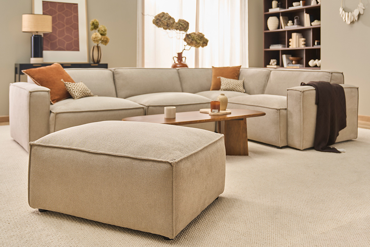 Pouf repose-pieds en tissu chenille beige avec canap� et table basse en arri�re-plan, vue en perspective.