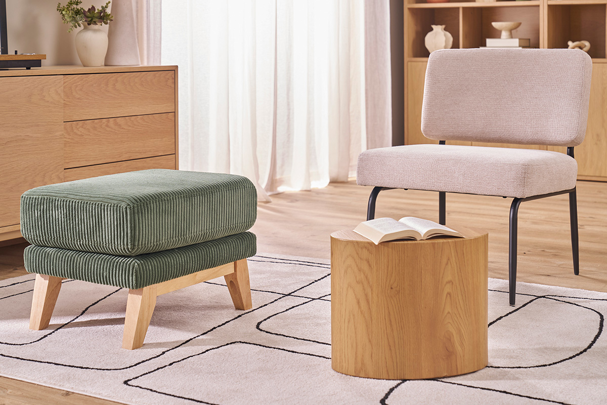 Pouf en tissu velours vert avec pieds en bois, vue de face, pr�s d'une table basse et d'un fauteuil.