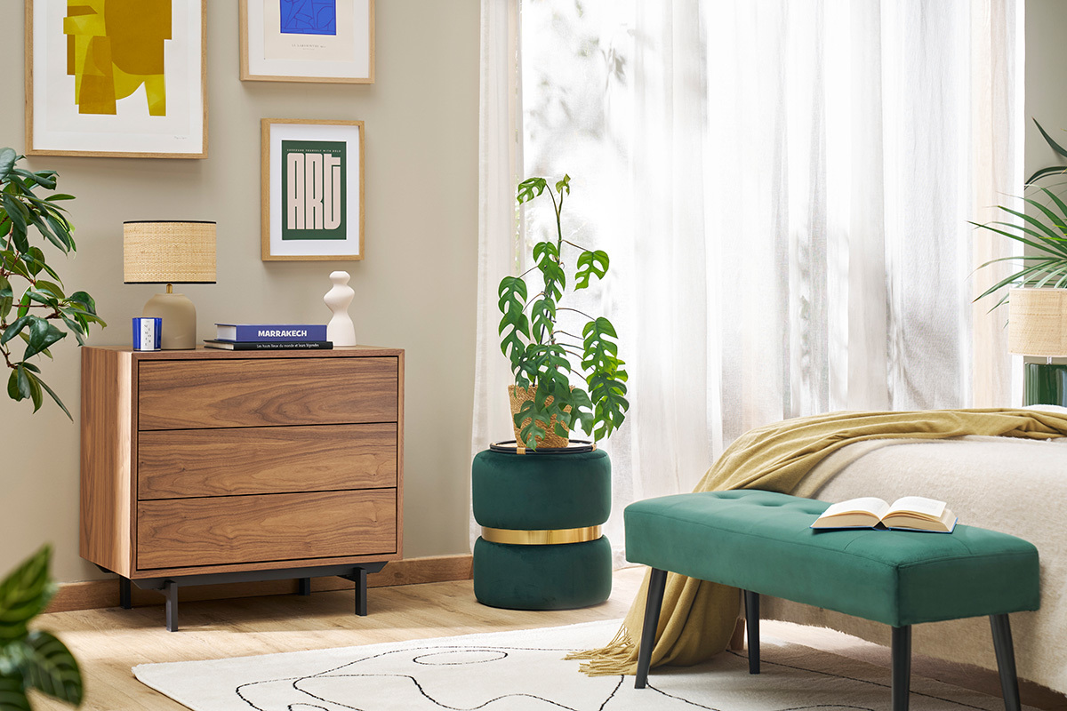 Pouf rond en velours vert, dans une chambre avec commode en bois et banc.