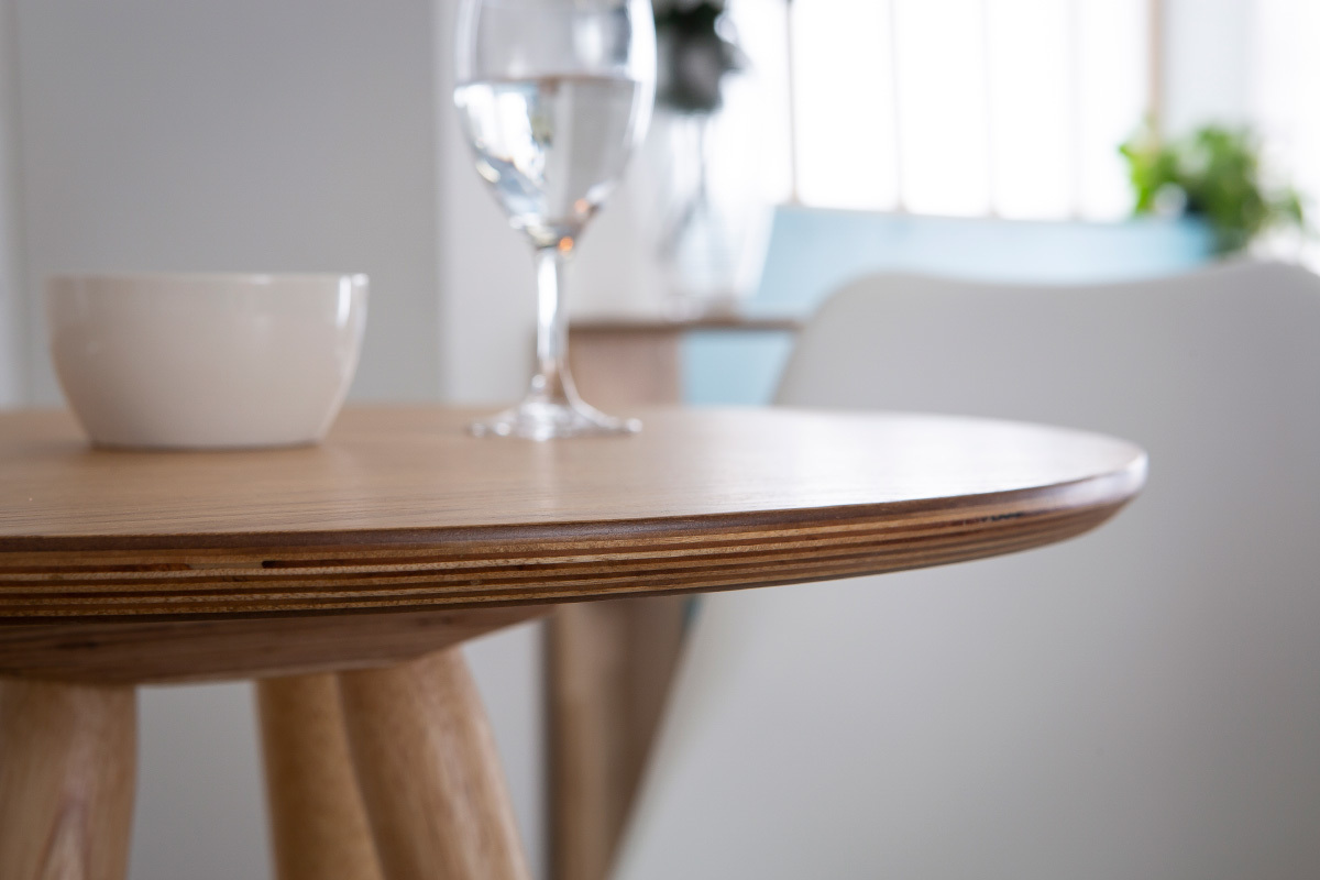 Table de bar ronde en bois scandinave de 60 cm, vue de pr�s avec un bol et un verre d'eau.